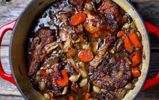 Red pot of coq-au-vin on a wooden table, a traditionally French dish to eat.