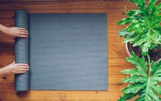 Hands rolling up a yoga mat next to large green, leafy plants.